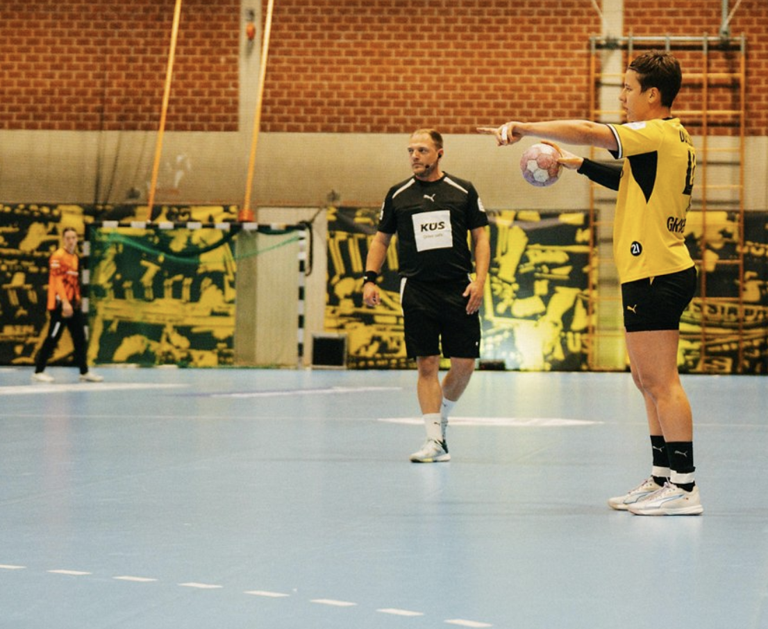 BVB-Handballerin Alina Grijseels dirigiert das Angriffsspiel am Kreis. Hinter ihr betrachten der Schiedsrichter und eine Torhüterin des BVB das Geschehen.