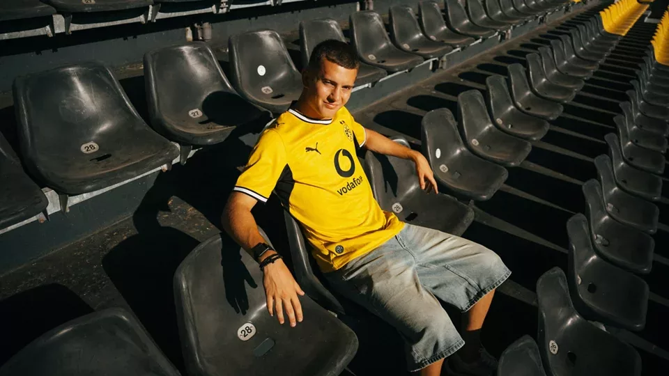 Kosta Karetsas sitzt mit in Shorts und dem neuen BVB-Heimtrikot, auf schwarzen Stühlen im Westfalenstadion