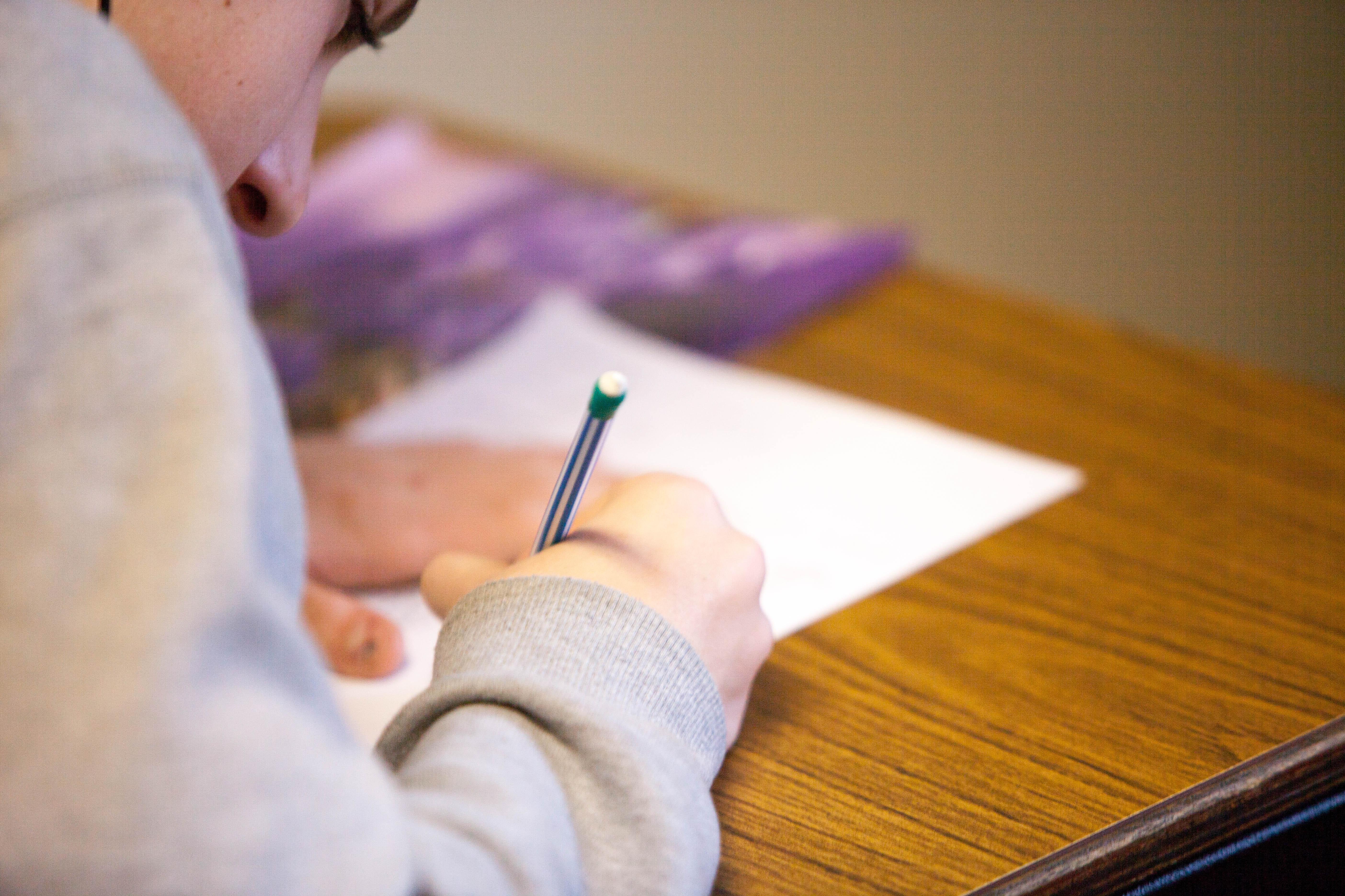 Ein männlicher Schüler sitzt am Tisch und füllt ein Blatt Papier mit seinem Stift aus